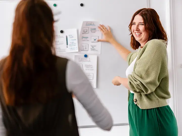 Frau hängt Zettel auf Whiteboard und lächelt